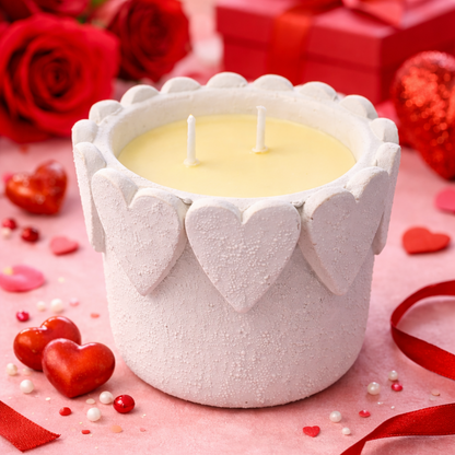 Candle in a heart-shaped container with red roses and ribbons on a pink background